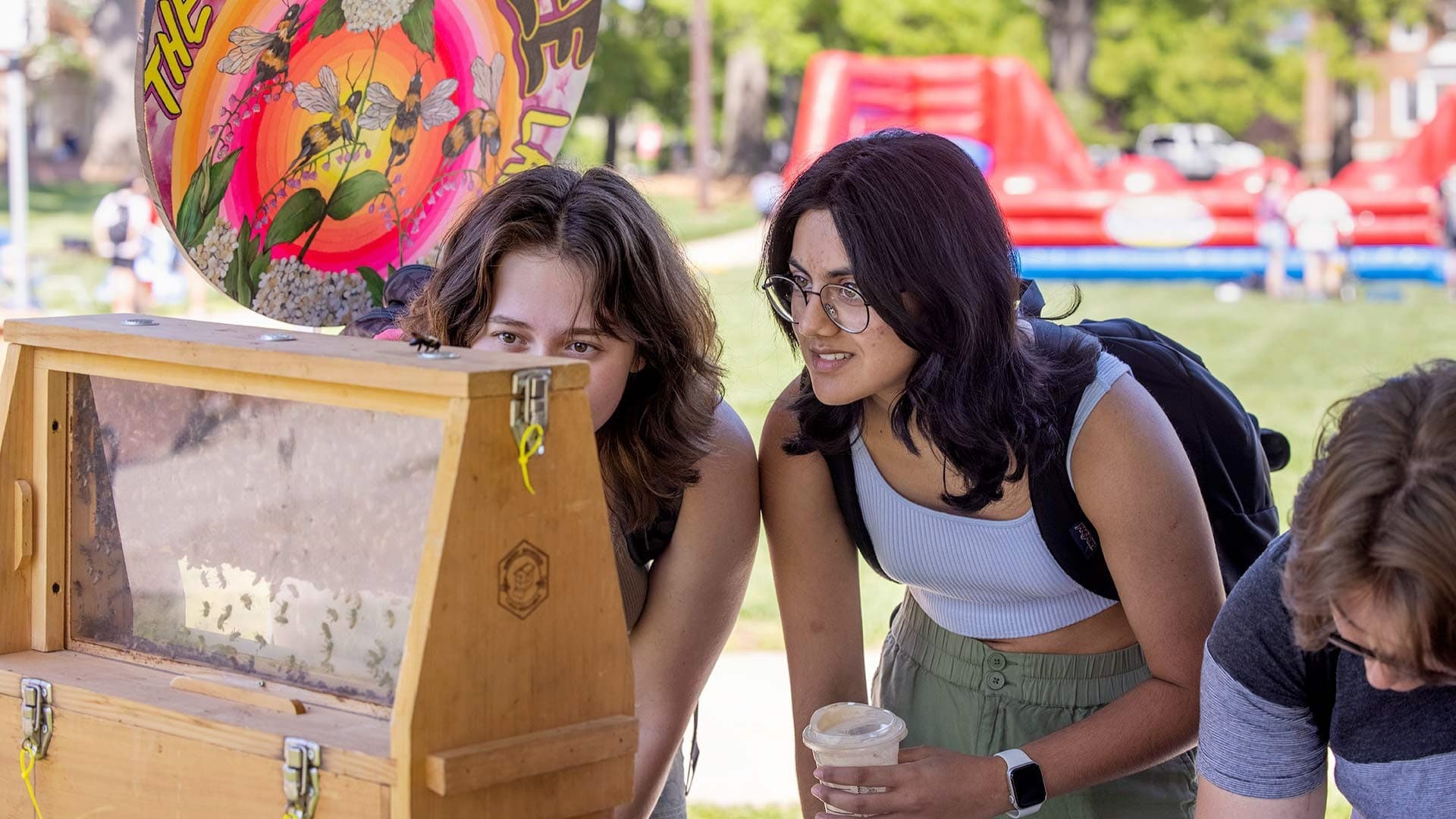 Natalie Wathen ’26, left, and Amudha Krishnan ’26 look for the queen bee in a beehive presented by UMD’s Honey Bee Lab. “Our campus just became a pollinator campus, which is a really big deal because it means we’re working toward making sure our campus is safe for pollinators,” said Kensie Olson ’22, a technician in the Honey Bee Lab.