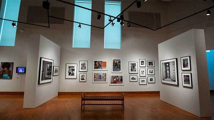 Crisp light walls display framed pieces of various media in an art gallery